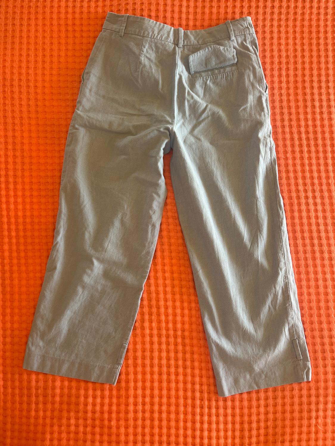 Light grey trousers, viewed from behind, with belt loops and a back pocket, laid out on a textured orange fabric background.