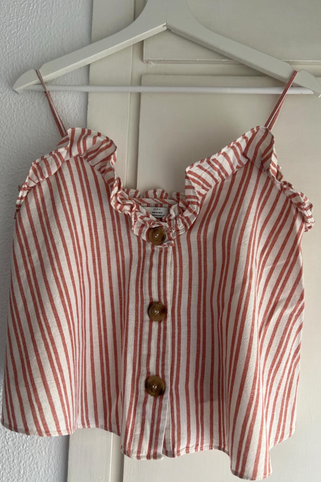 Front view of a red and white striped camisole top with front buttons and frills on the neckline.