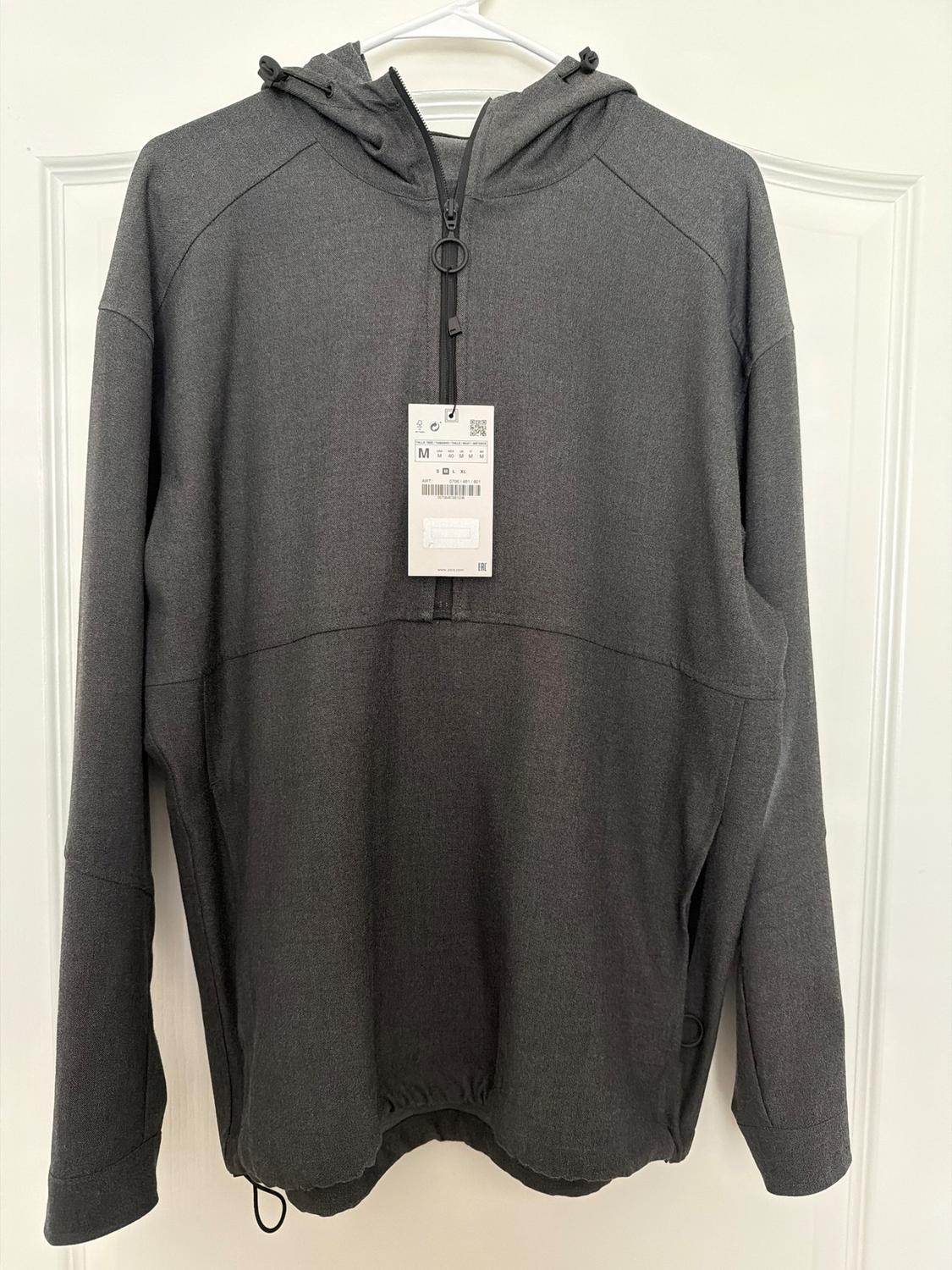 Gray hooded zip-up sweatshirt, hanging on a white hanger. Visible tag with product details in the center.