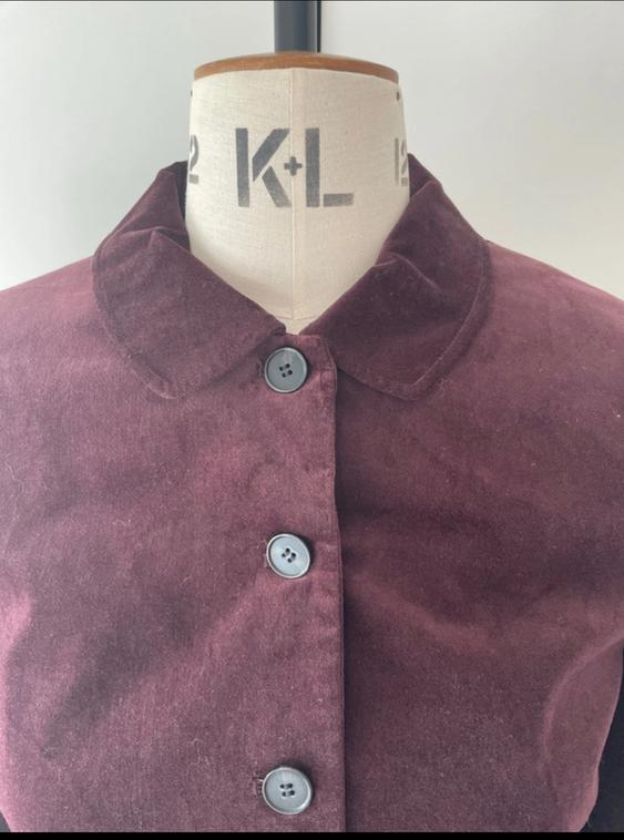 Mannequin with a burgundy velvet jacket, round neck, and black buttons. Visible text: "K+L". White background.