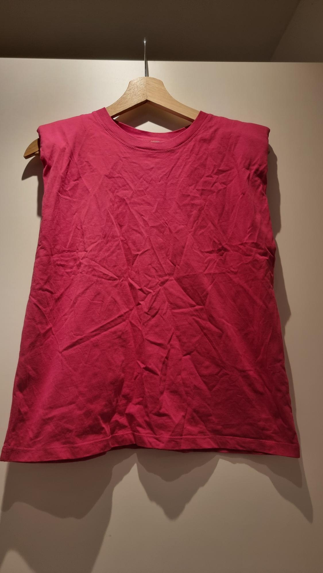 Pink sleeveless top hanging on a wooden hanger against a beige background. The fabric is creased.