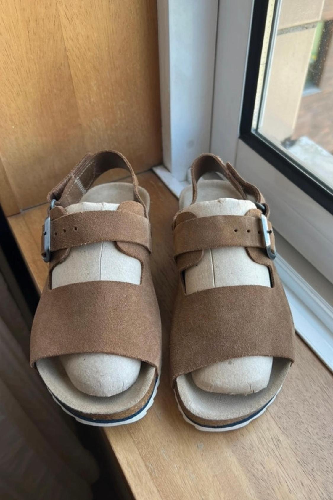 Front view of brown sandals with buckle and white sole.