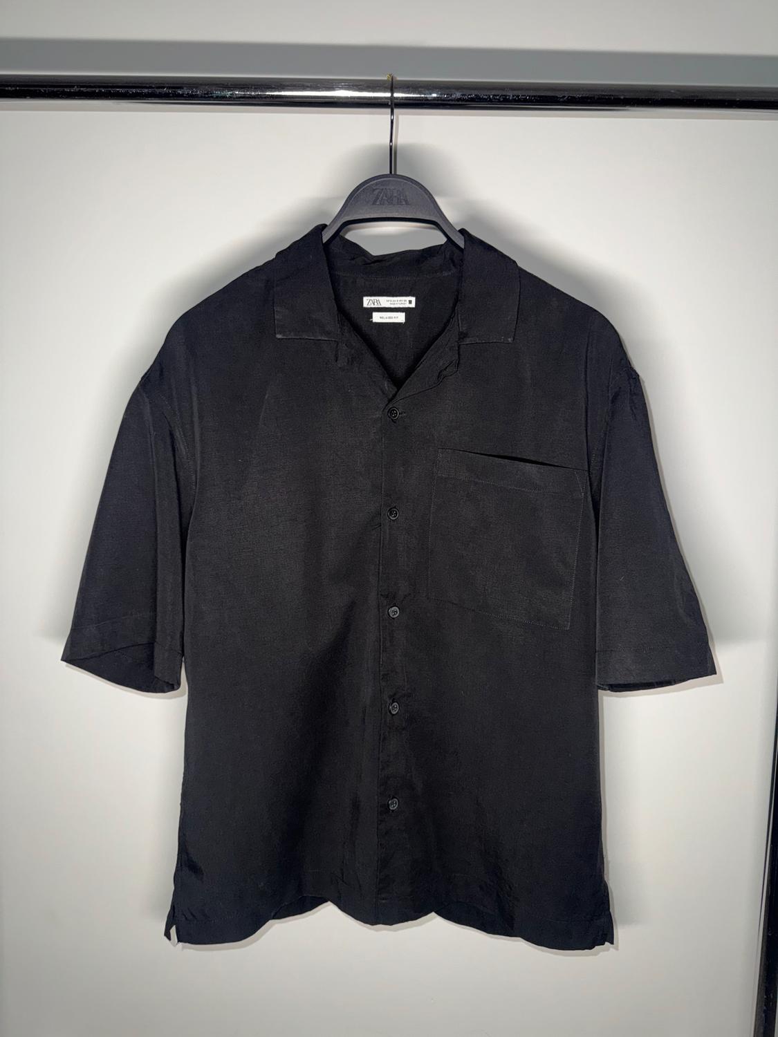 Black short-sleeved shirt hanging on a black hanger with the label visible, on a white background.