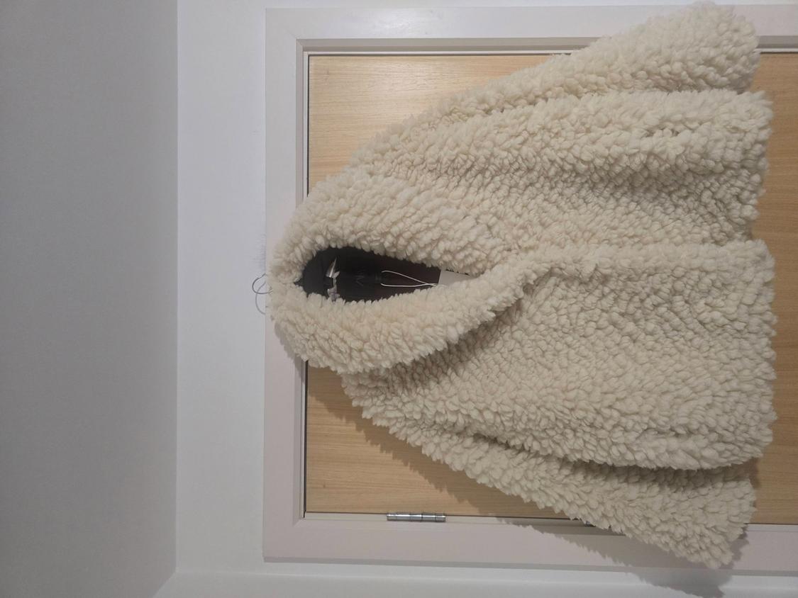 Beige wool jacket hanging on a light wooden door. The texture is fluffy and bulky.