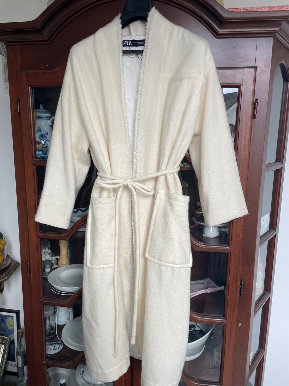 White coat hanging on a hanger in front of a wooden cabinet with glass doors, displaying plates and decorations inside.