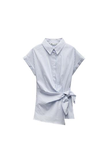 Short-sleeve blue and white striped shirt on a white background. Features a collar, buttons, and a front knot. Label text: ZARA.