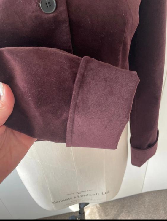 Hand holding the sleeve of a burgundy velvet jacket with a black button, on a Kennett & Lindsell Ltd mannequin.
