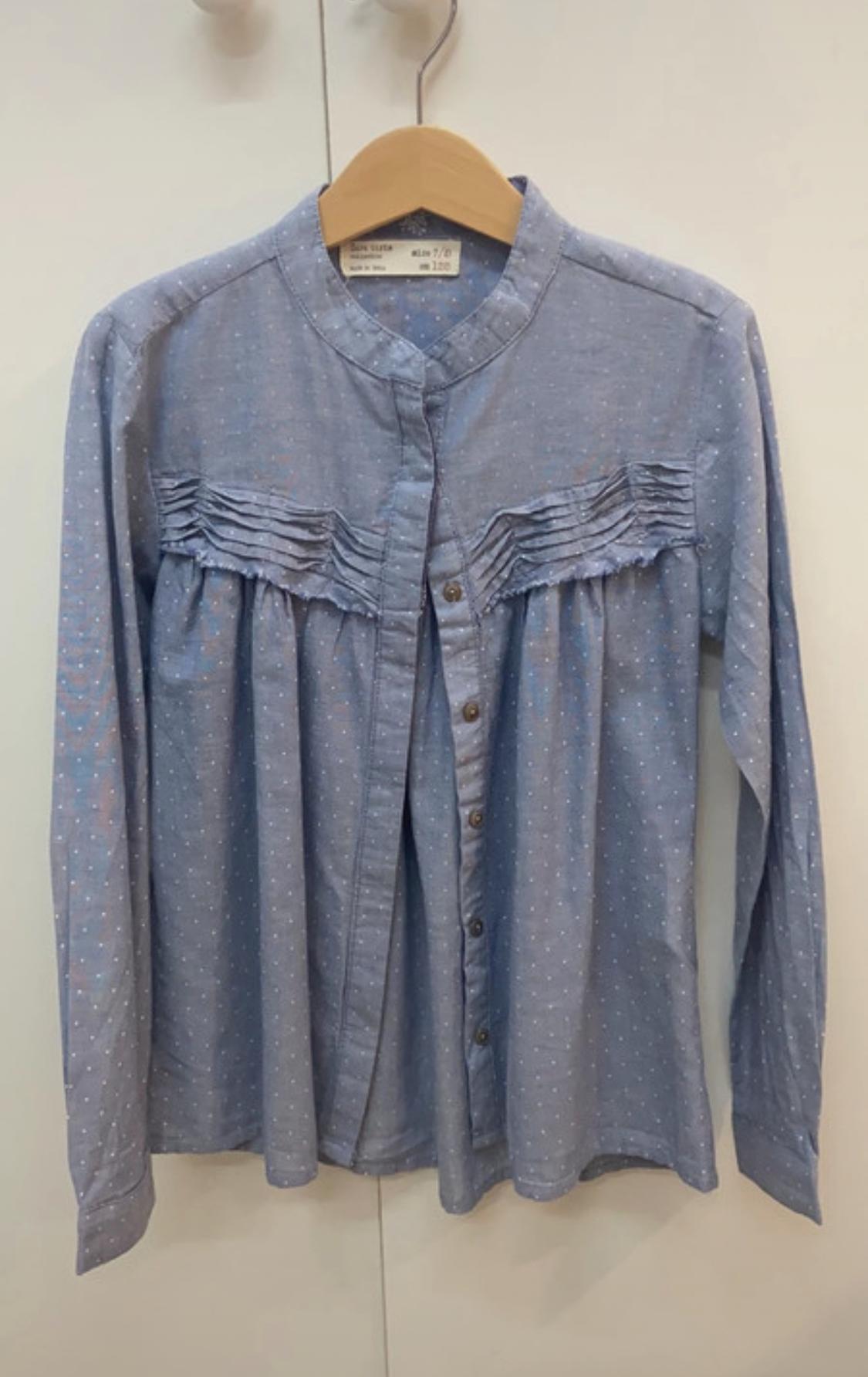 Front view of a blue shirt with white polka dots, a mandarin collar and pleats on the chest, button fastening.