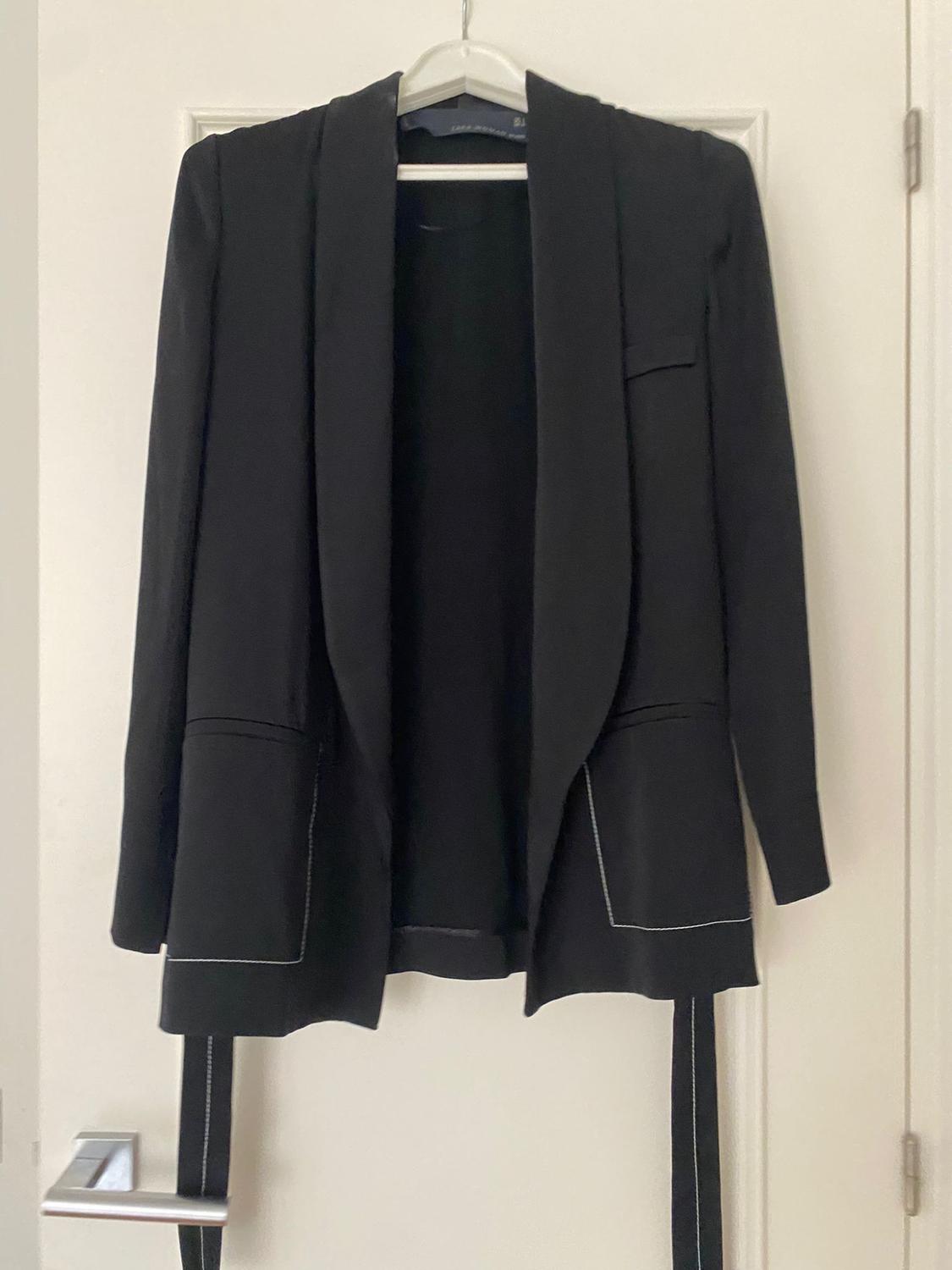 Black jacket hanging on a hanger over a white door. Stitching details visible on the pockets and sleeves.
