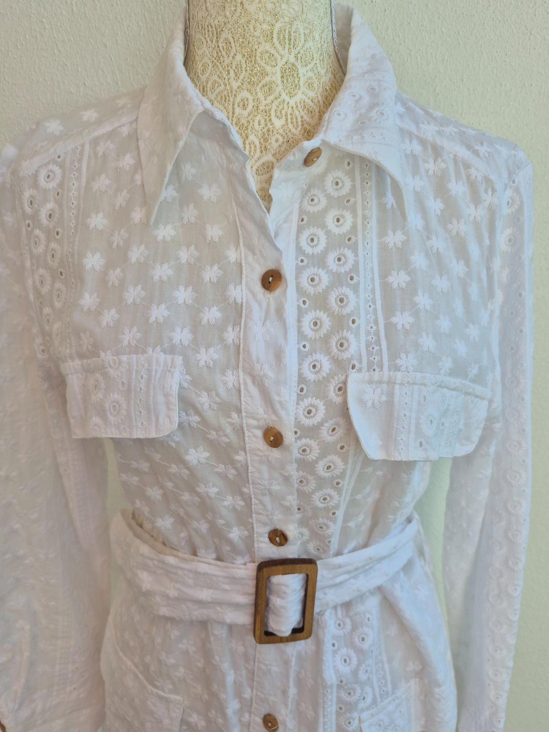 Embroidered white dress with flowers, wooden buttons, and a belt with a square buckle. Displayed on a lace mannequin.