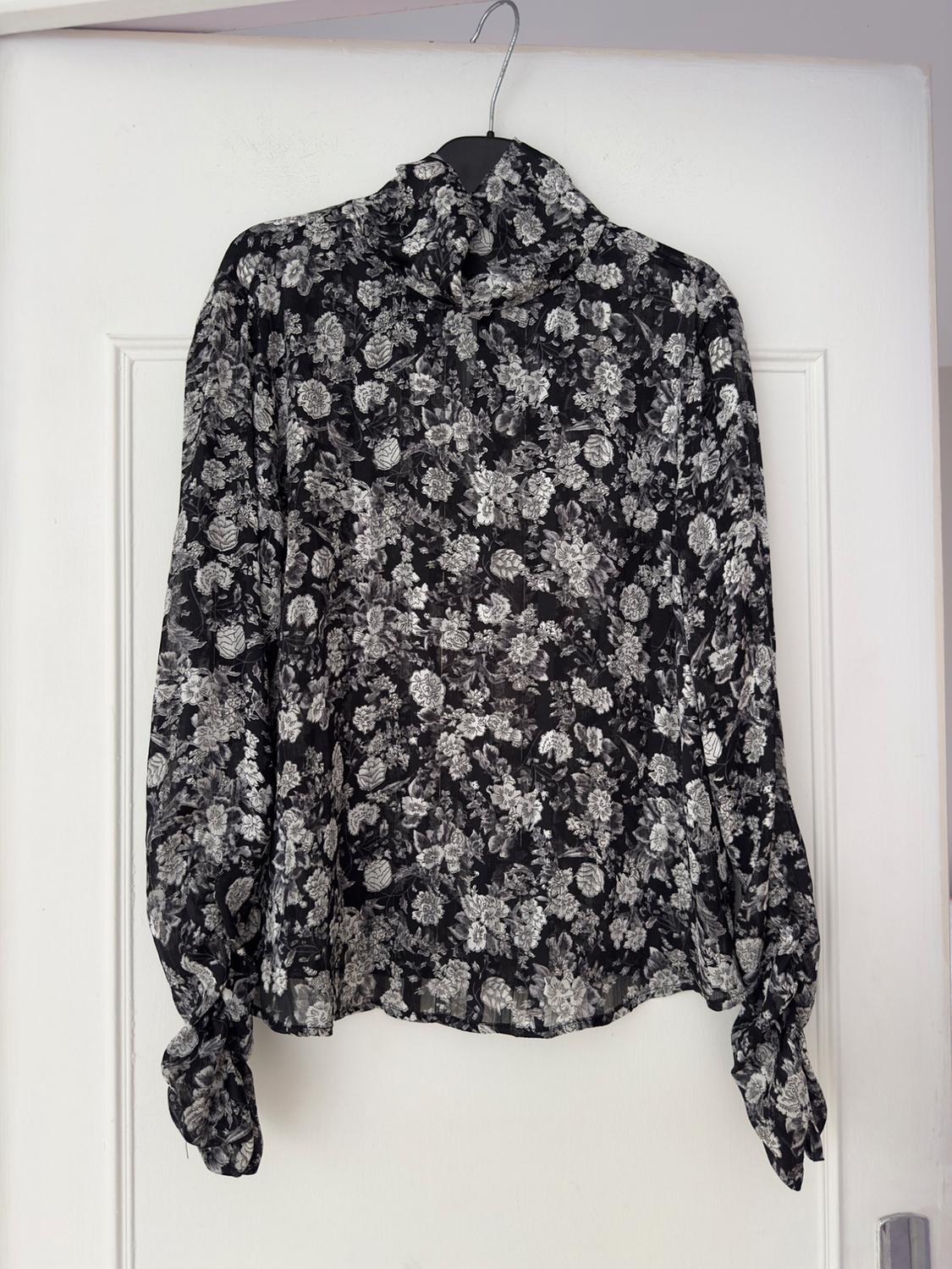 Black and white floral print long-sleeved blouse, hanging on a hanger over a white door.