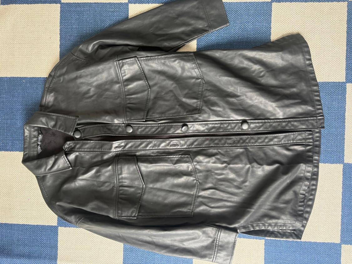 Black leather jacket with large pockets and front buttons, on a blue and beige checkered rug.