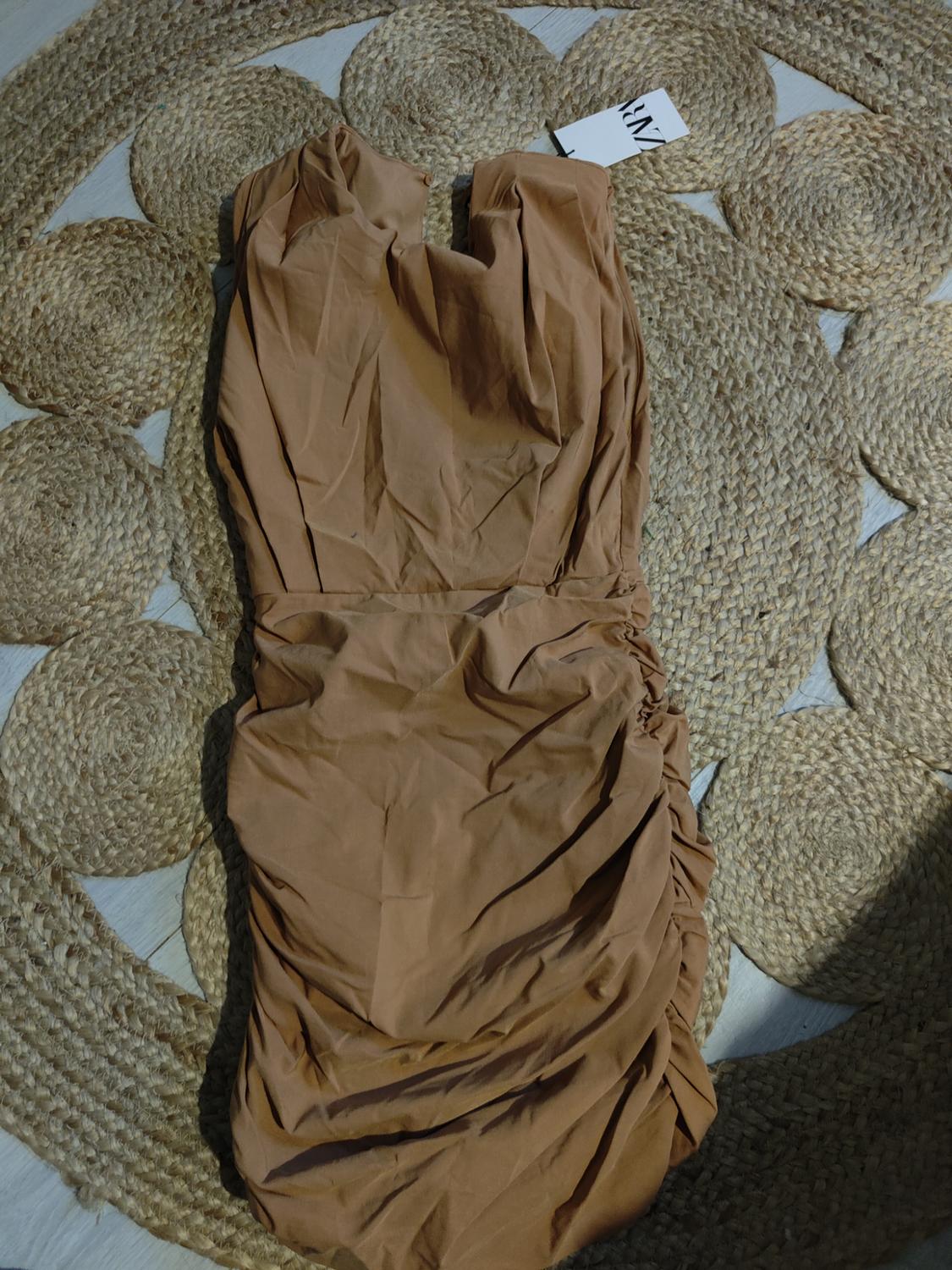 Creased brown dress on a braided jute rug. Visible tag with "Zara" text. Relaxed and natural atmosphere.