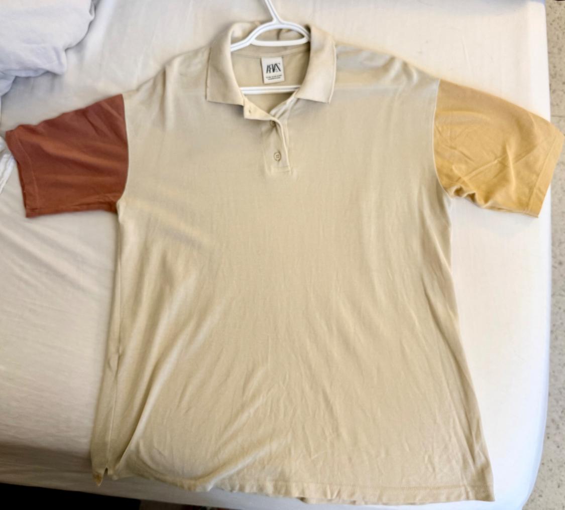Beige polo shirt with different coloured sleeves, one brown and one yellow, on a white bed. Visible label on the collar.