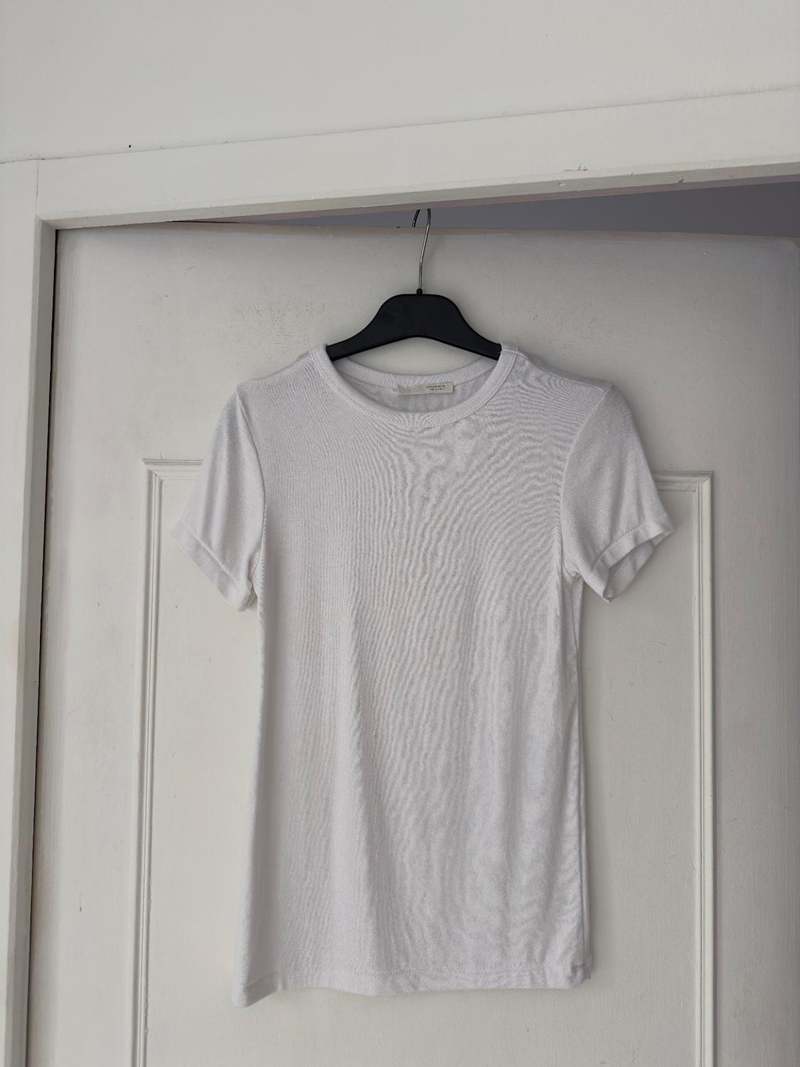 White short-sleeved t-shirt hanging on a black hanger over a white door. The fabric texture is visible.