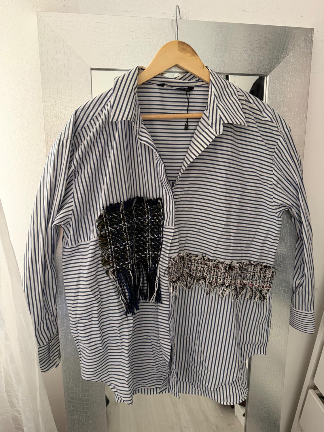 Black and white striped shirt hanging on a wooden hanger, with textured fabric details on the chest and waist.