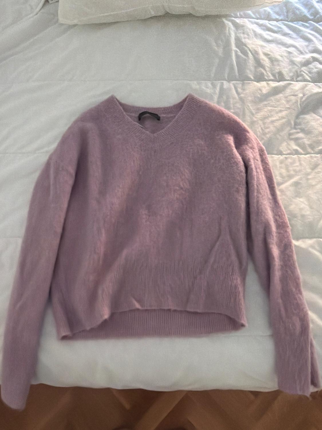 Lilac V-neck knitted jumper, spread out on a white bed.