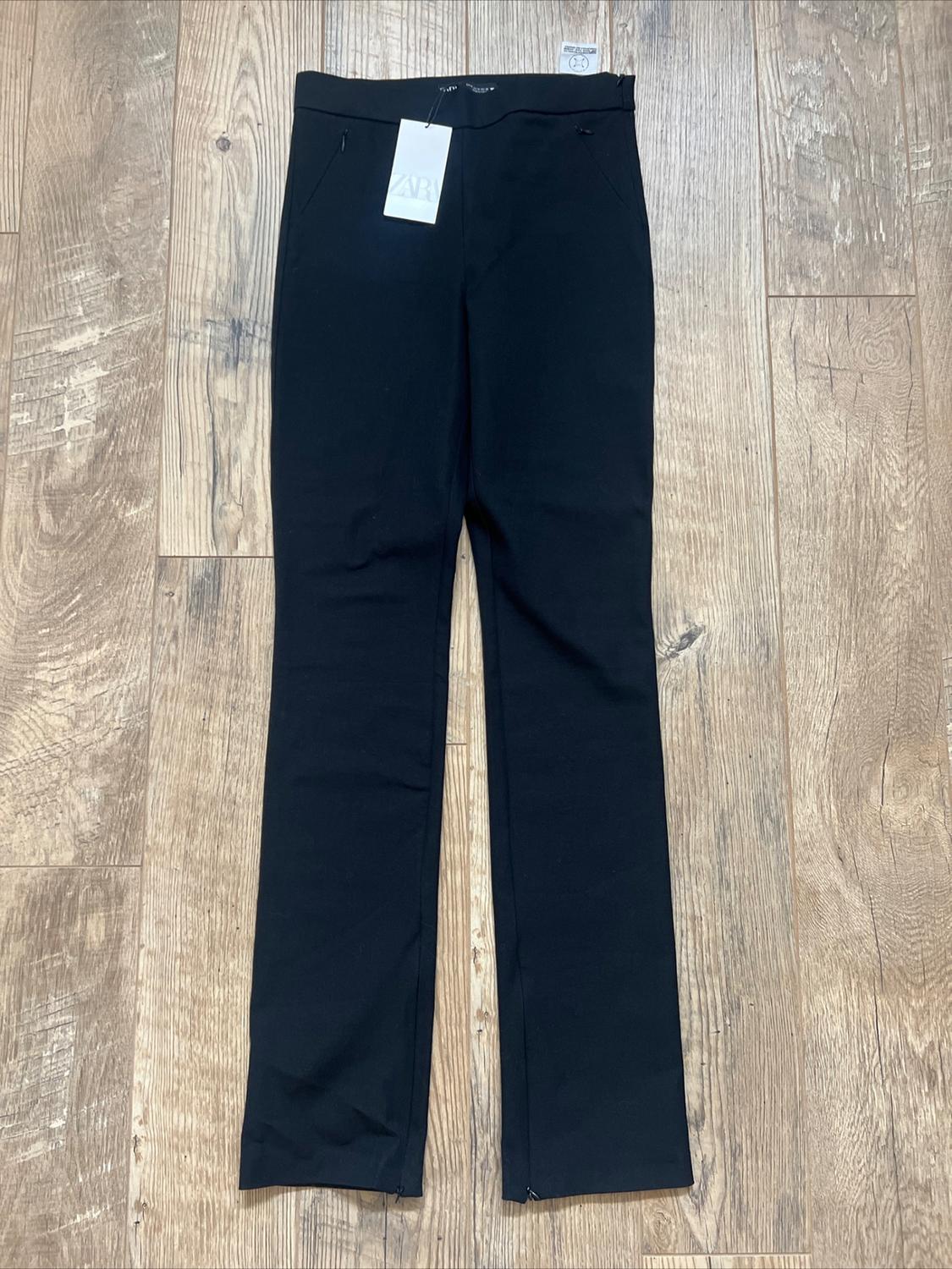 Black pants on light wood floor, with visible tag that says "ZARA".