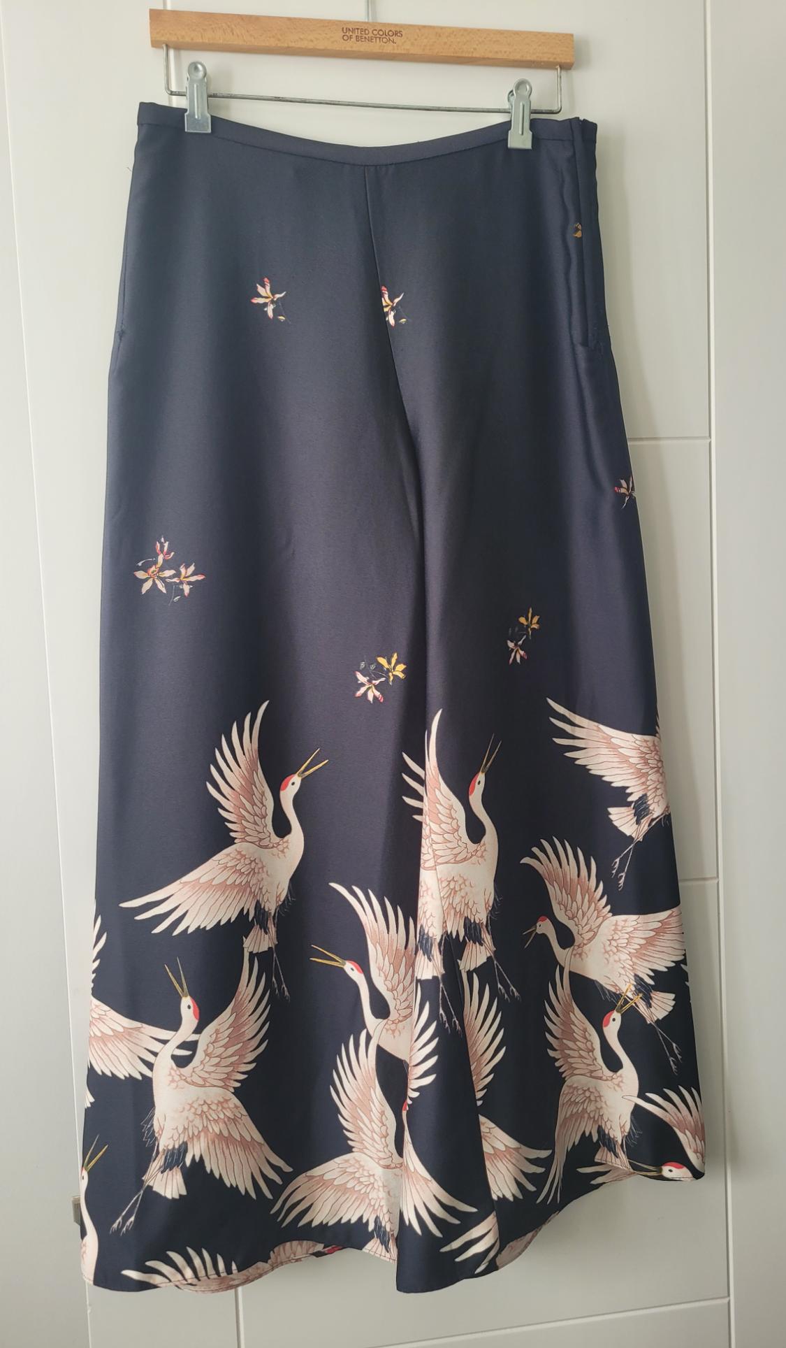 Blue skirt with a white crane and pink floral print, hanging on a wooden hanger from United Colors of Benetton.