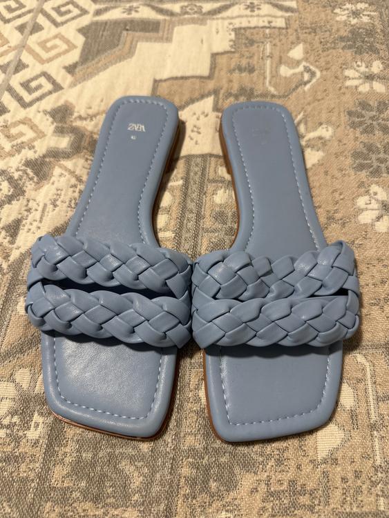 Blue flat sandals with braided straps on a geometric design rug. Visible text: "ZARA 40".