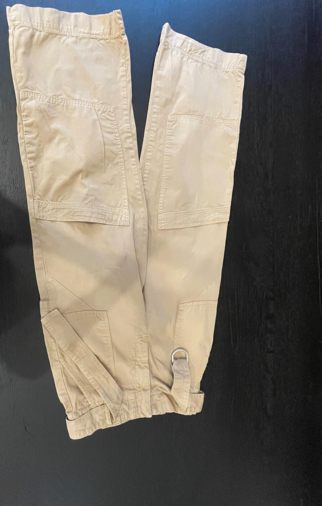 Beige cargo trousers with large pockets and a belt with a metal buckle, laid out on a flat dark wood surface.