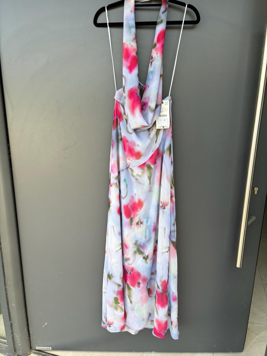 Long dress with a pink and green floral print, hanging on a black coat hanger in front of a grey door bearing the text HORMANN.