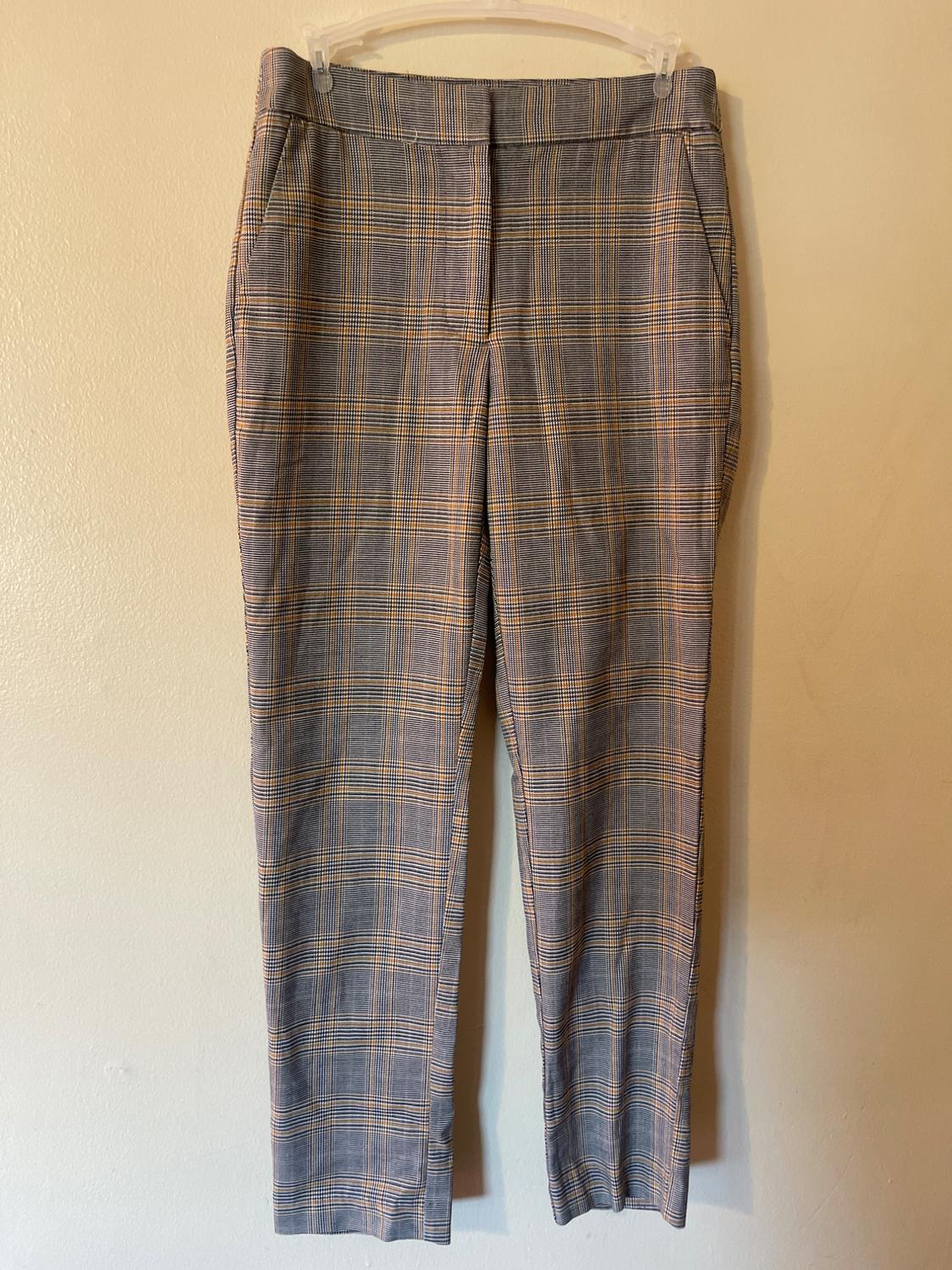 Gray and yellow plaid pants hanging on a clear hanger against a beige wall.