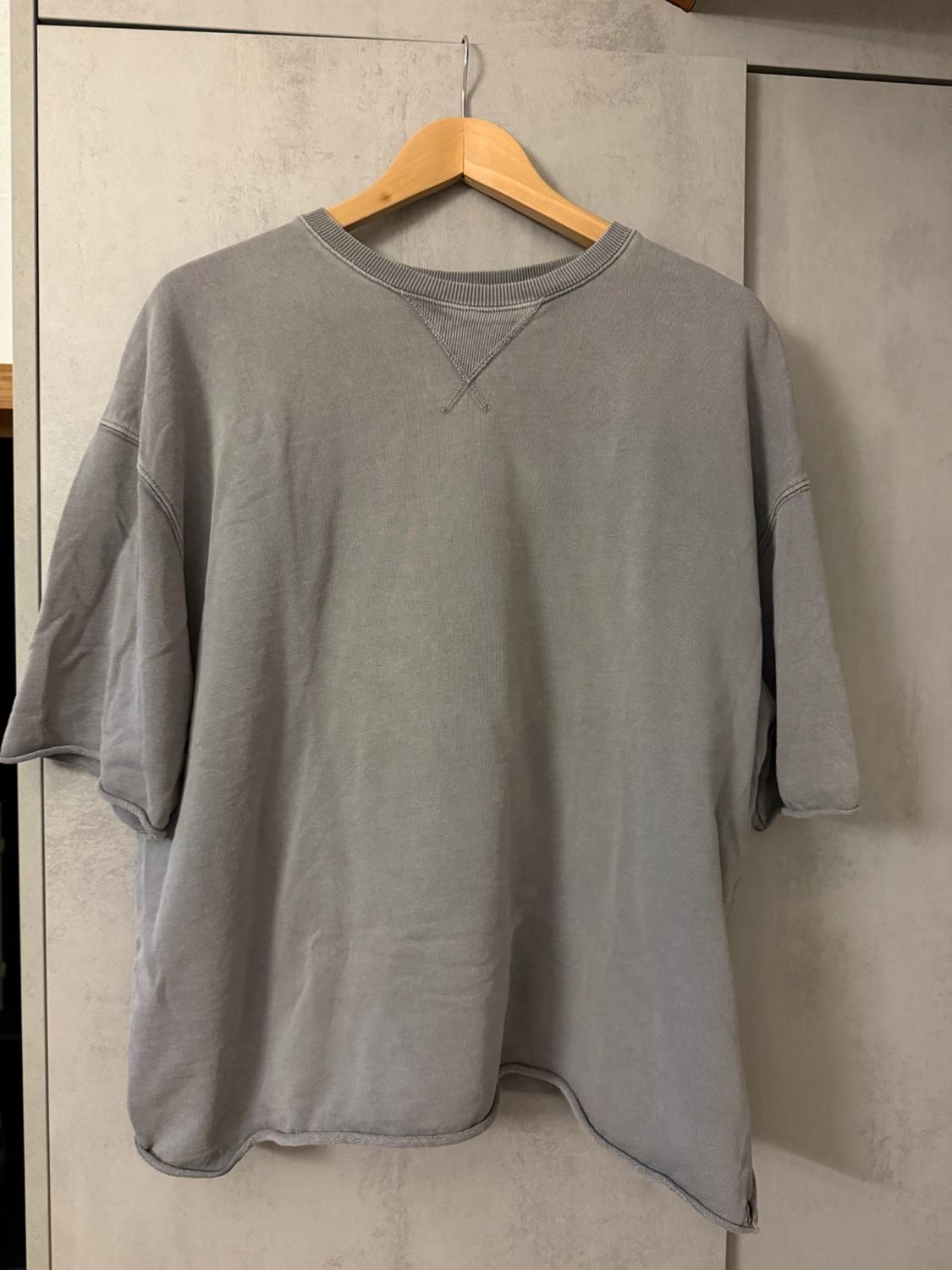 Grey short-sleeved T-shirt hanging on a wooden hanger against a beige wardrobe background.