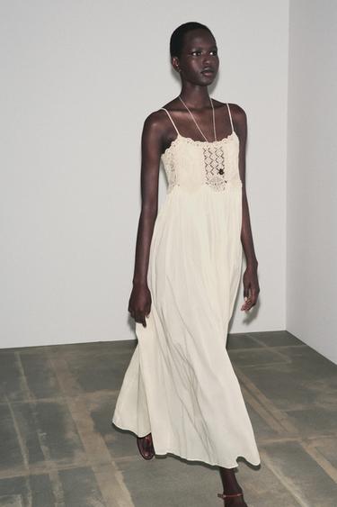 Komplet dlouhých šatů v surové barvě s výstřihem bez ramínek, tenkými ramínky a krajkovým detailem na hrudi.