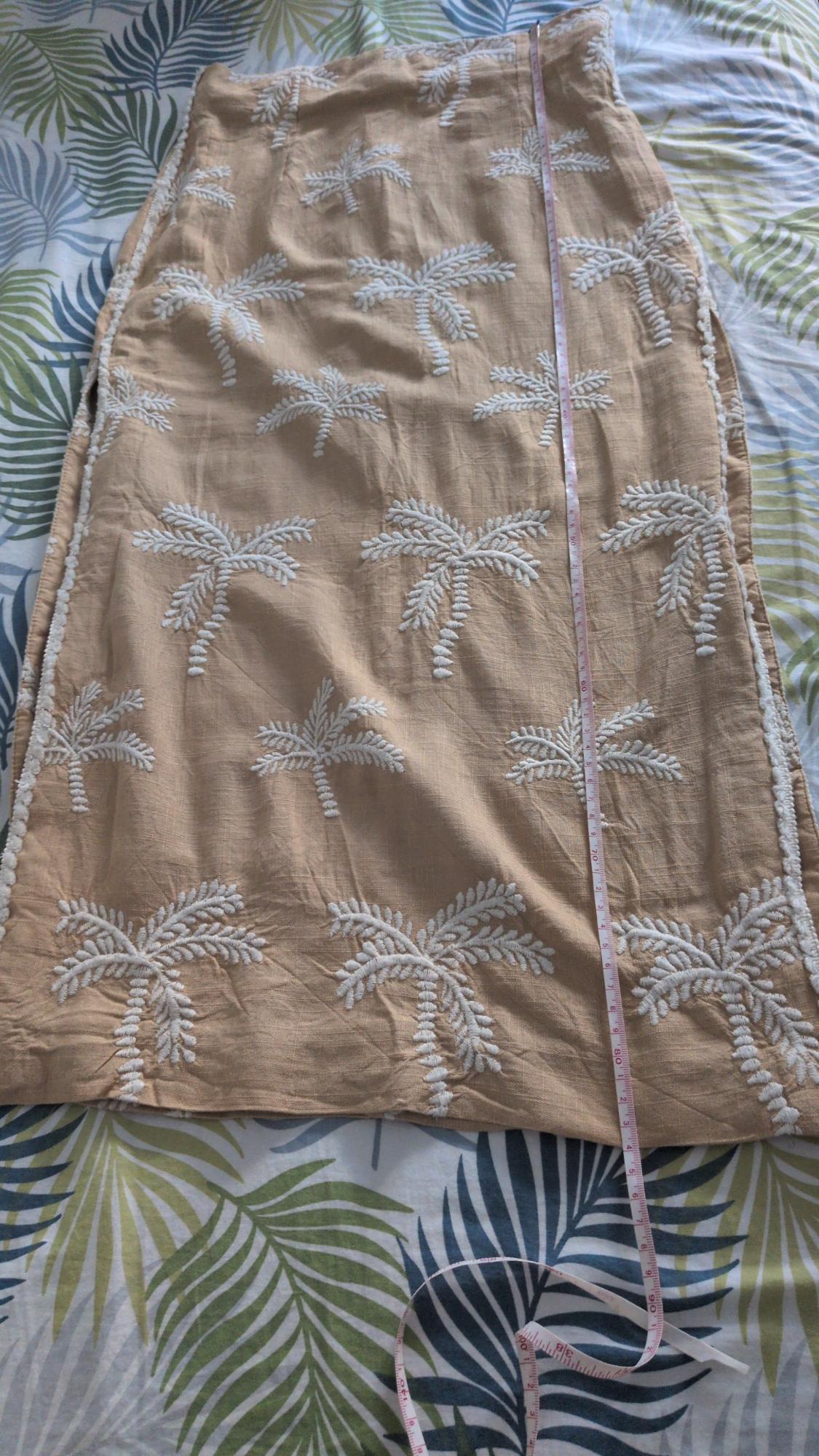 Beige skirt with white embroidered palm trees on tropical leaf print fabric, with a pink tape measure laid out on top.
