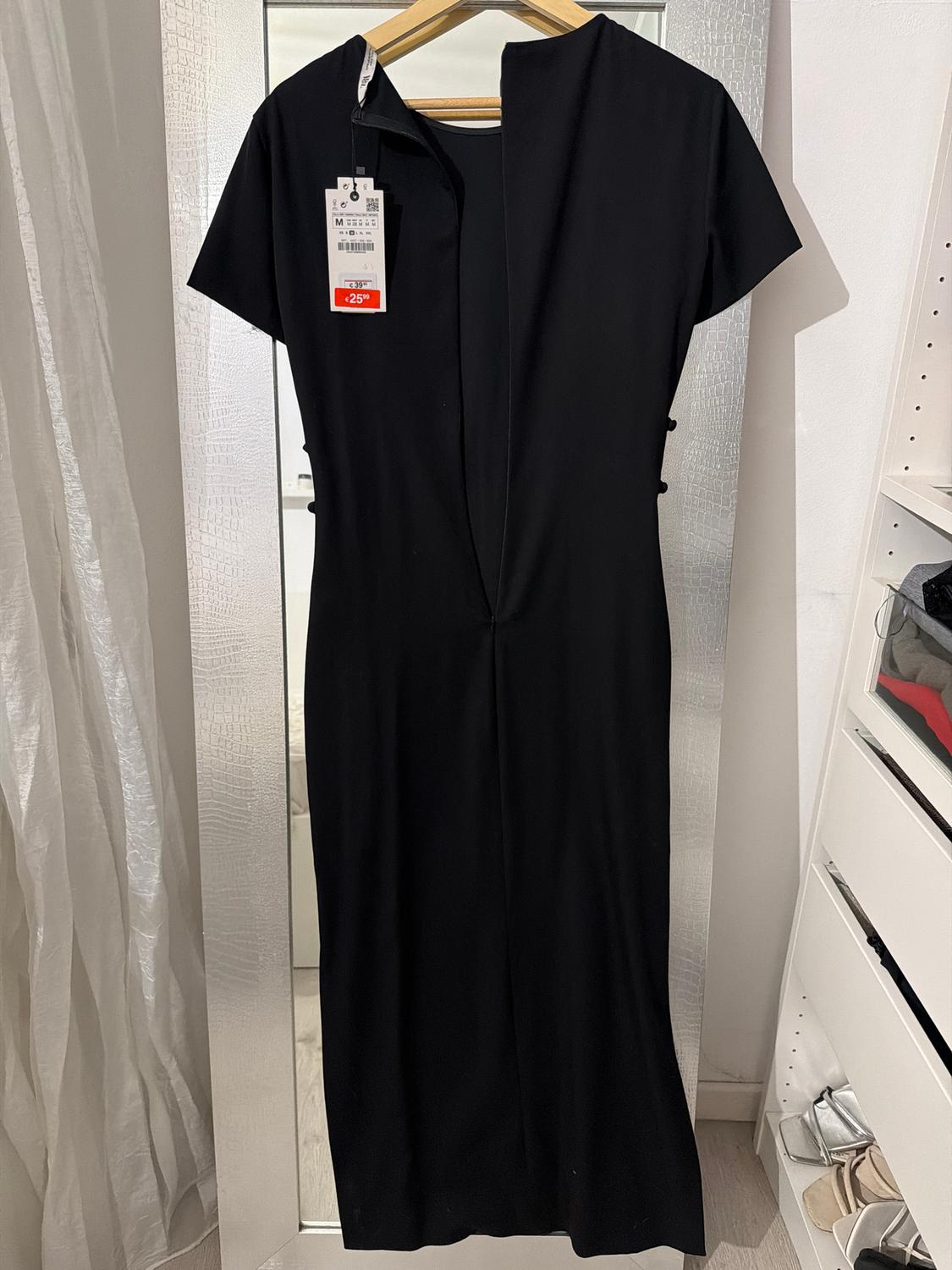Short-sleeved black dress hanging on a hanger, with a 25% discount tag. Mirror and white curtain background.