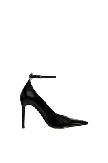 Black high-heeled shoe with a glossy finish, pointed toe, and buckled ankle strap, shown in profile against a white background.