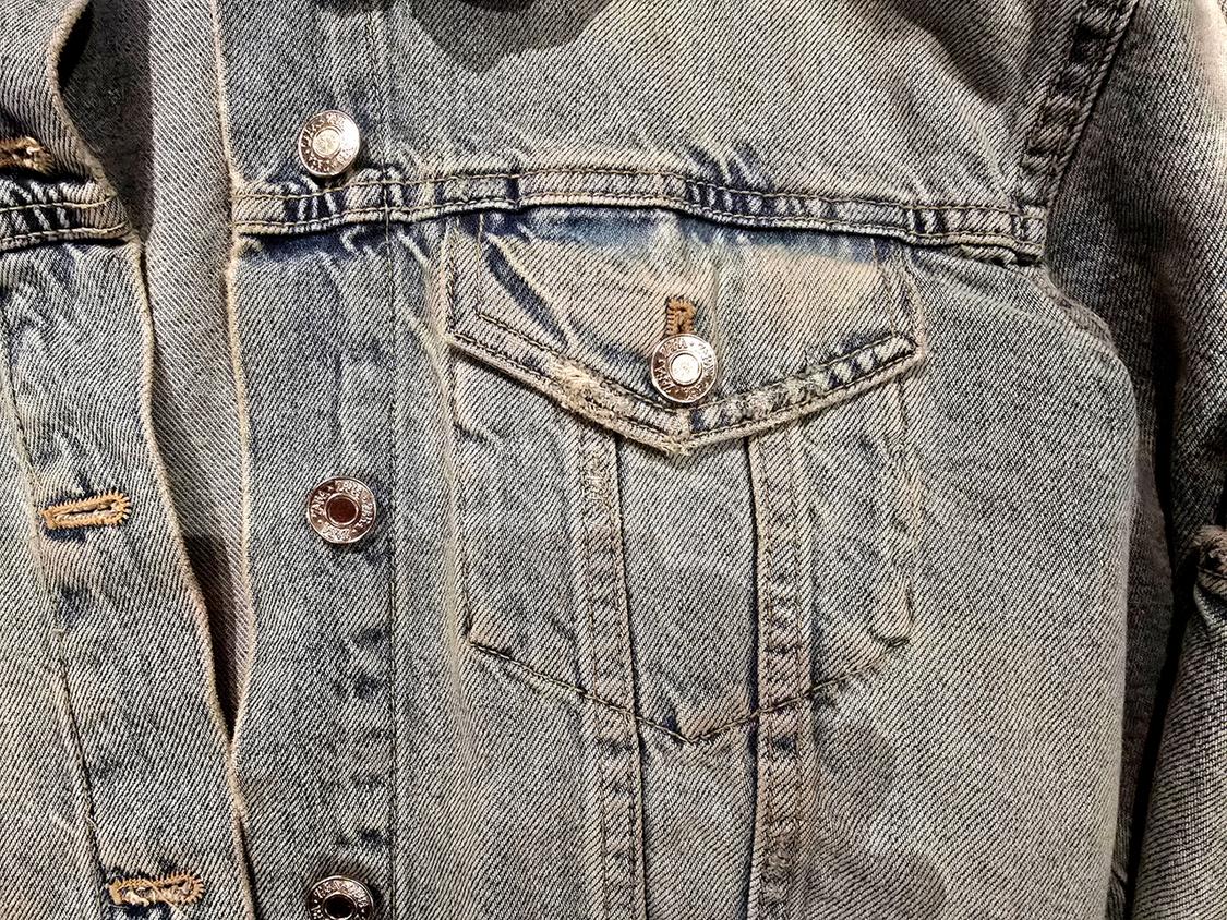 Light blue denim jacket with metallic buttons and chest pocket. Worn fabric with visible seams.