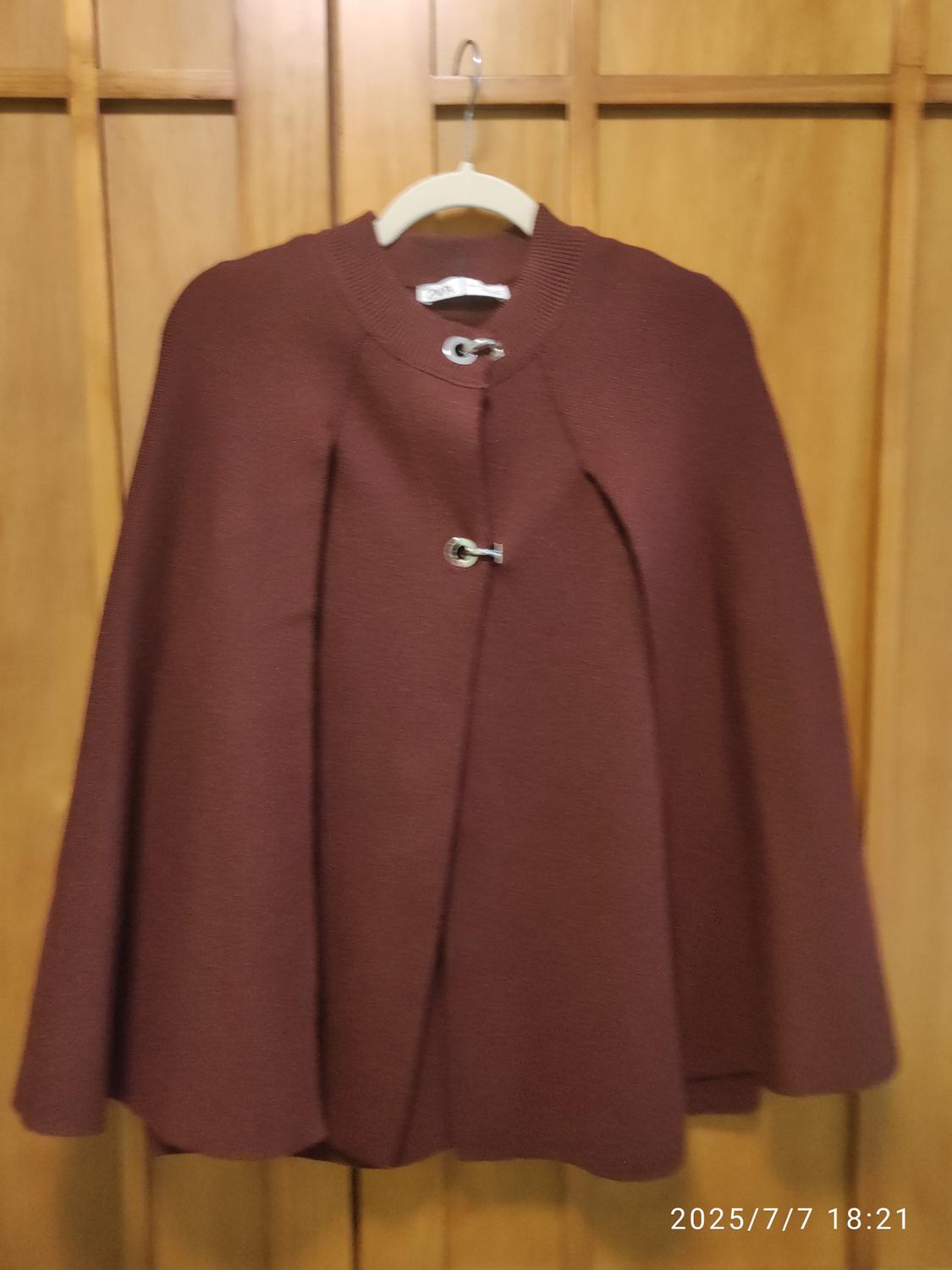 Brown cloak with a metal clasp at the neck, hanging on a hanger in front of a wooden door. Date visible: 2025/7/7 18:21.