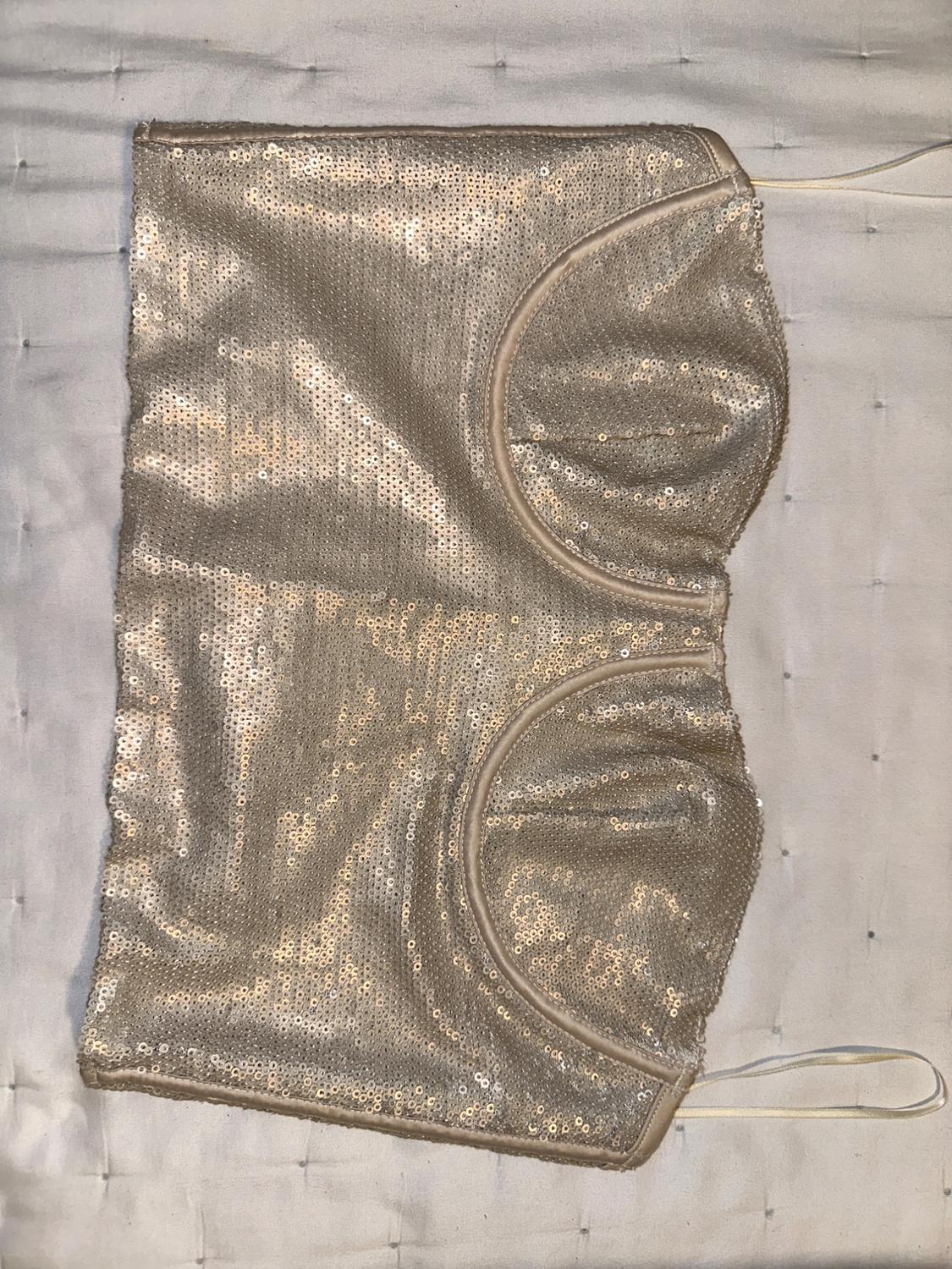Gold sequin top on a white padded surface. Strapless design with defined cups and fine elastic.