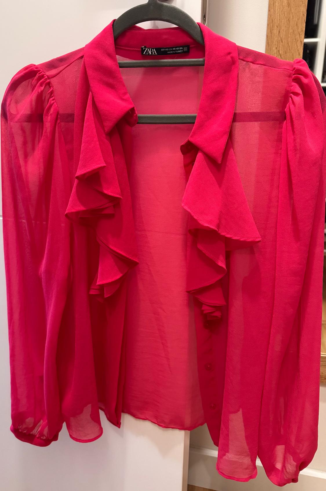 Sheer red blouse with front ruffles and long puff sleeves, hanging on a black hanger.