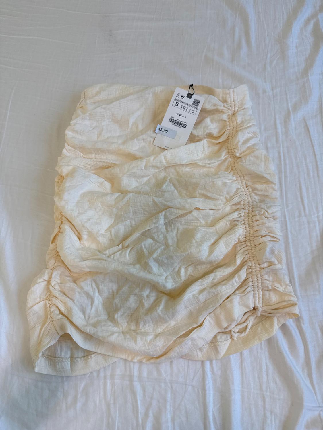 Beige ruched skirt on a white bed, with a visible price tag of 15.90 euros and size S.