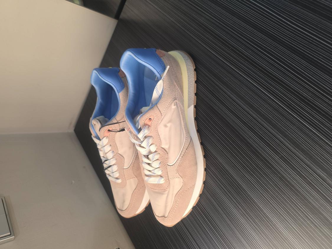 Beige trainers with blue details and a brown sole on a black striped background.