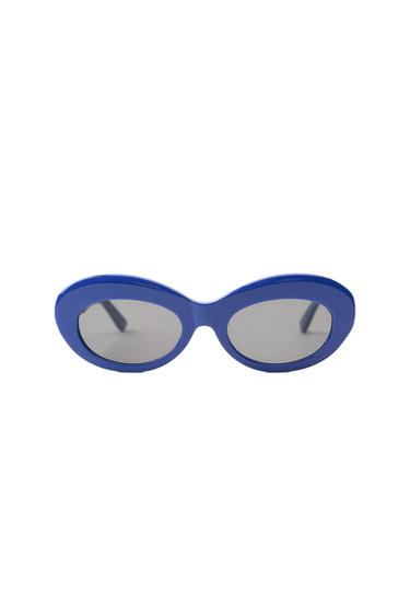 Thick-framed oval sunglasses in blue with gray-tinted lenses, displayed on a minimalist white background.