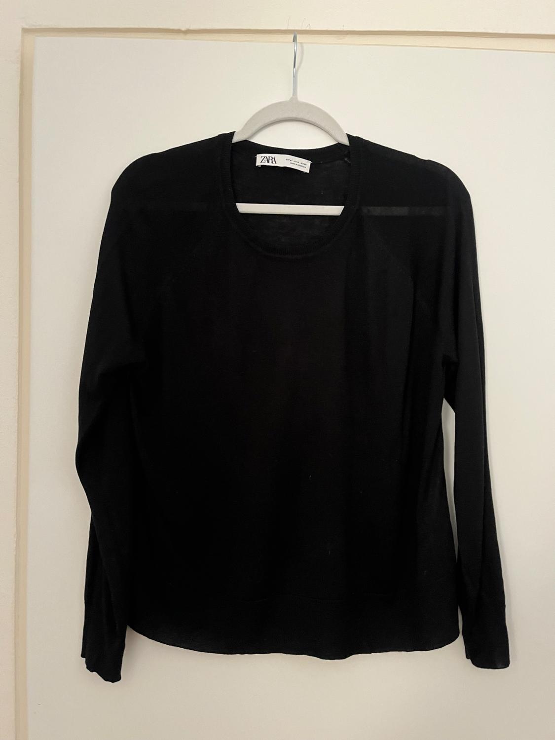 Black long-sleeved jumper hanging on a white hanger against a light background. Visible label with text "ZARA".