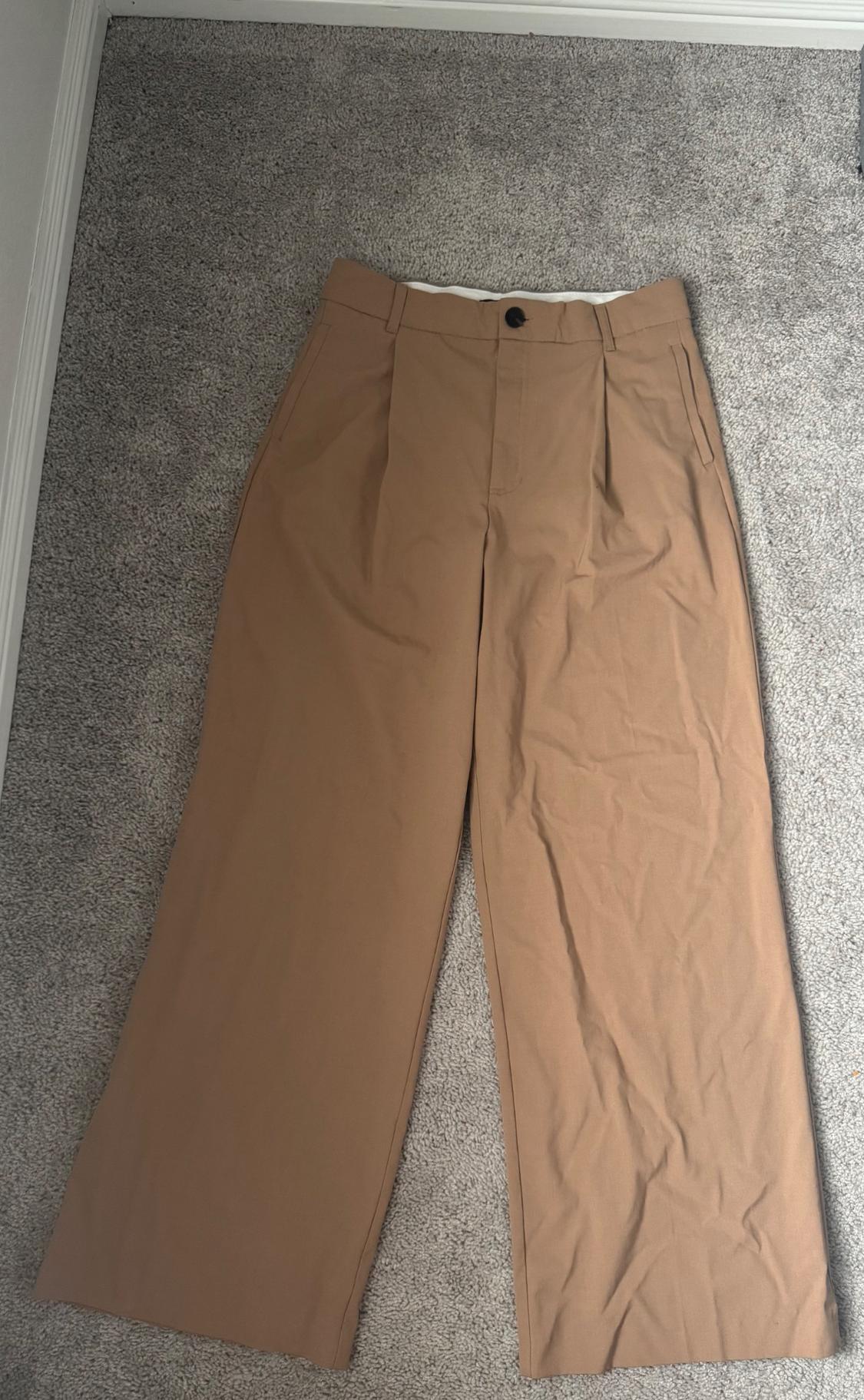 Front view of brown pleated pants with side pockets.