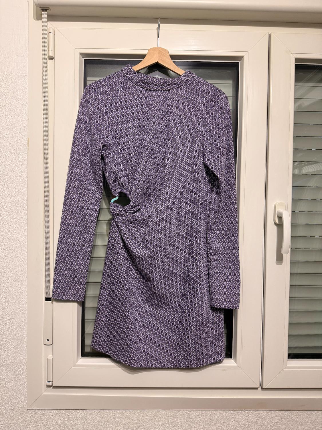 Purple dress with geometric print and ruched detail at the waist, hanging on a hanger in front of a white window.