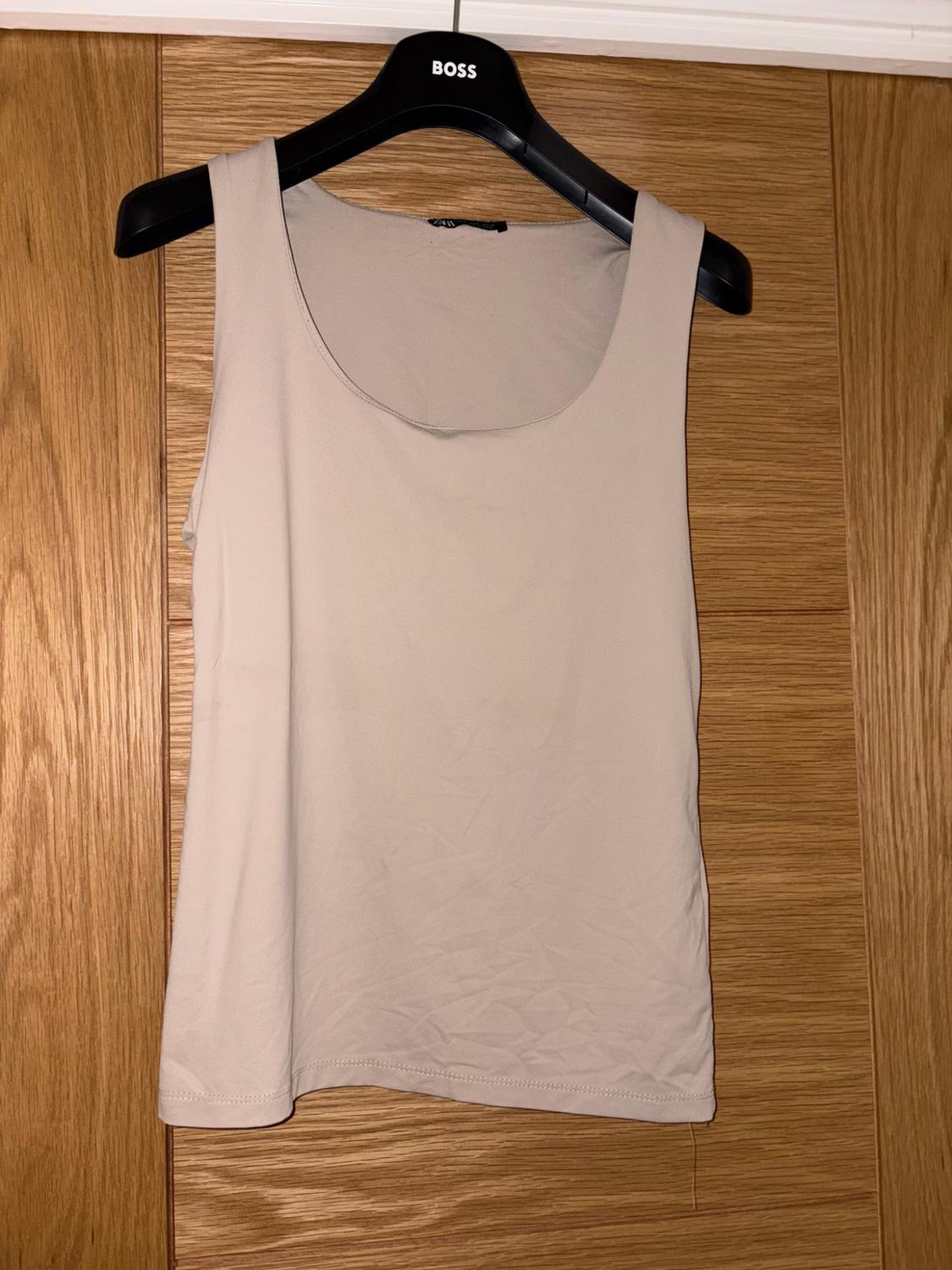 Beige vest top hanging on a black coat hanger with the text BOSS, on a wooden background.