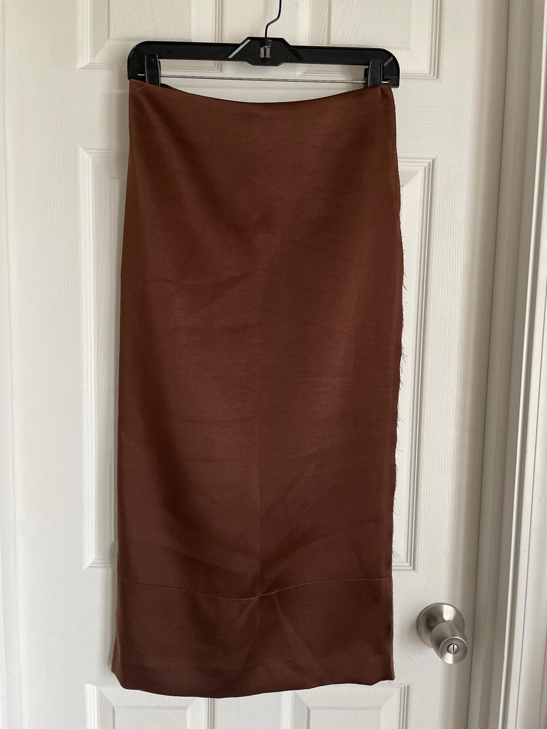 Brown skirt hanging on a black hanger over a white door. Smooth fabric and straight drape.