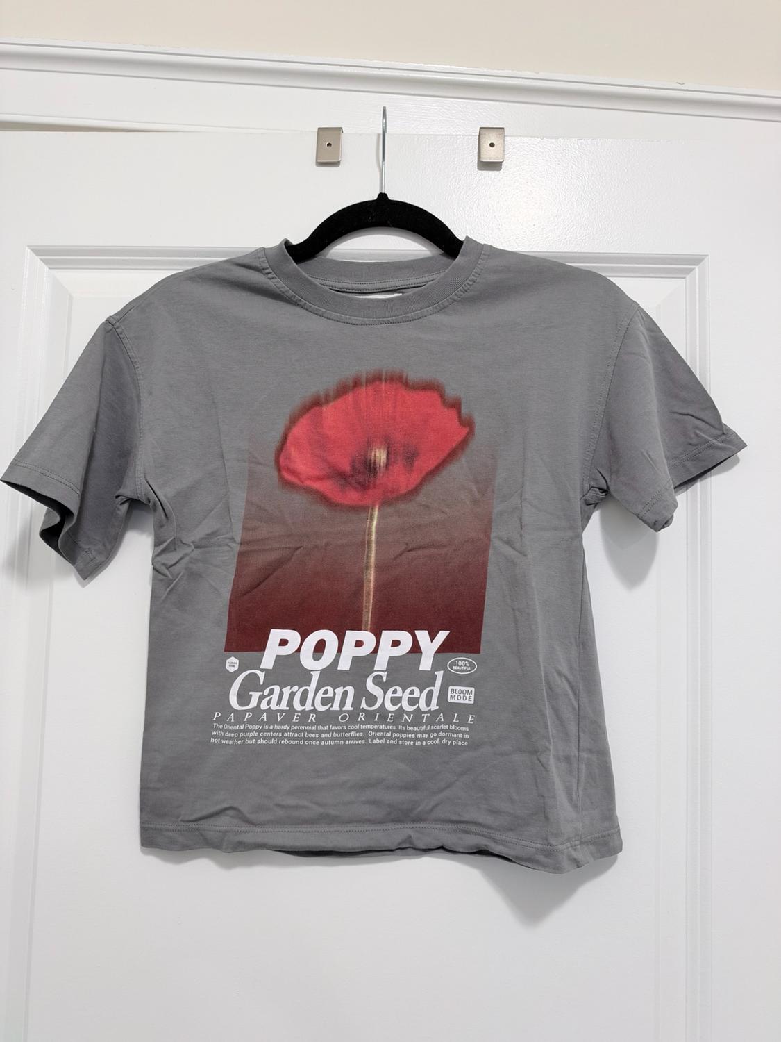 Gray t-shirt hanging on a white door. Red flower print and text: POPPY Garden Seed PAPAVER ORIENTALE.