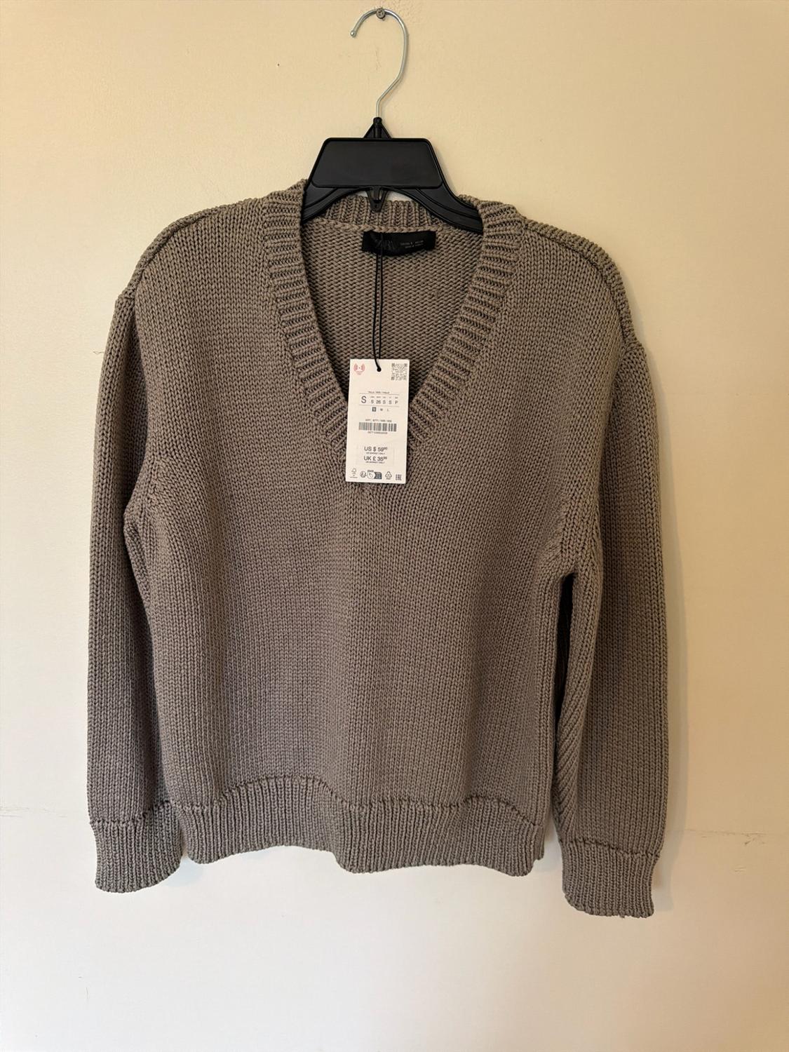 Beige knit V-neck sweater hanging on a black hanger against a light wall. Tag with text ZARA, S, US $ 59.90, UK £ 35.99.