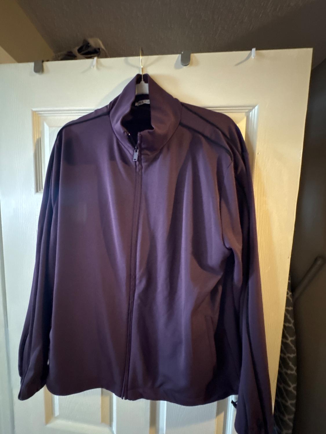 Purple jacket hanging on a white door, with a front zip and high collar. Indoor setting with soft light.
