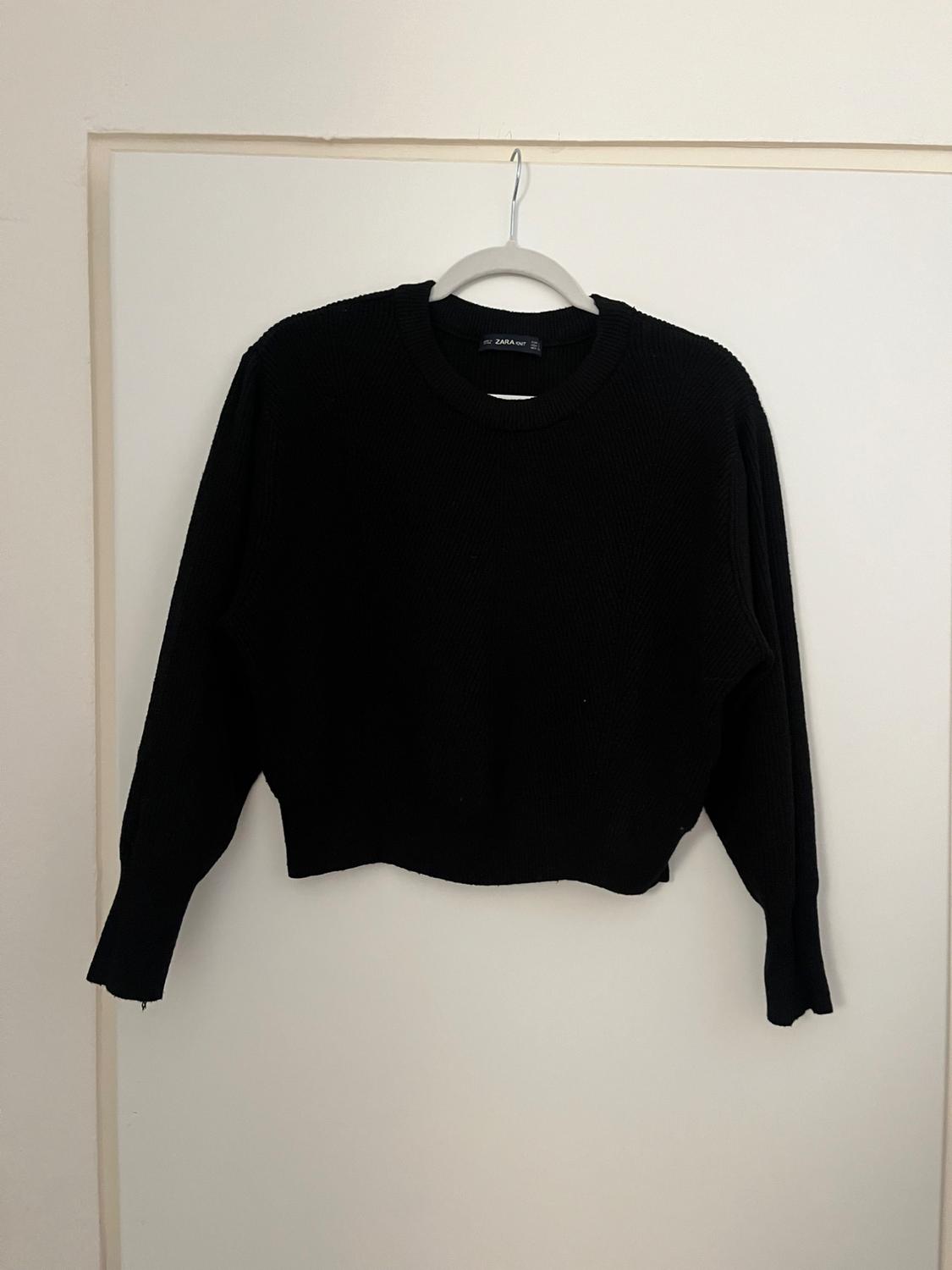Black jumper hanging on a white hanger against a light background. The label reads "ZARA".