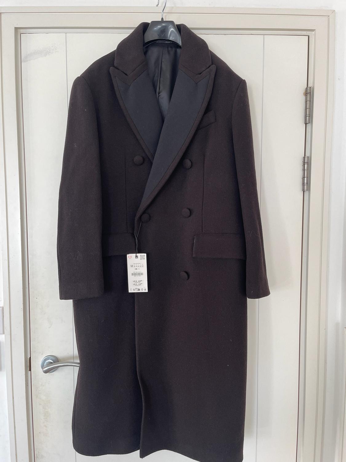 Dark brown double-breasted long coat hanging on a white door. Label with text: M, US $ 229.