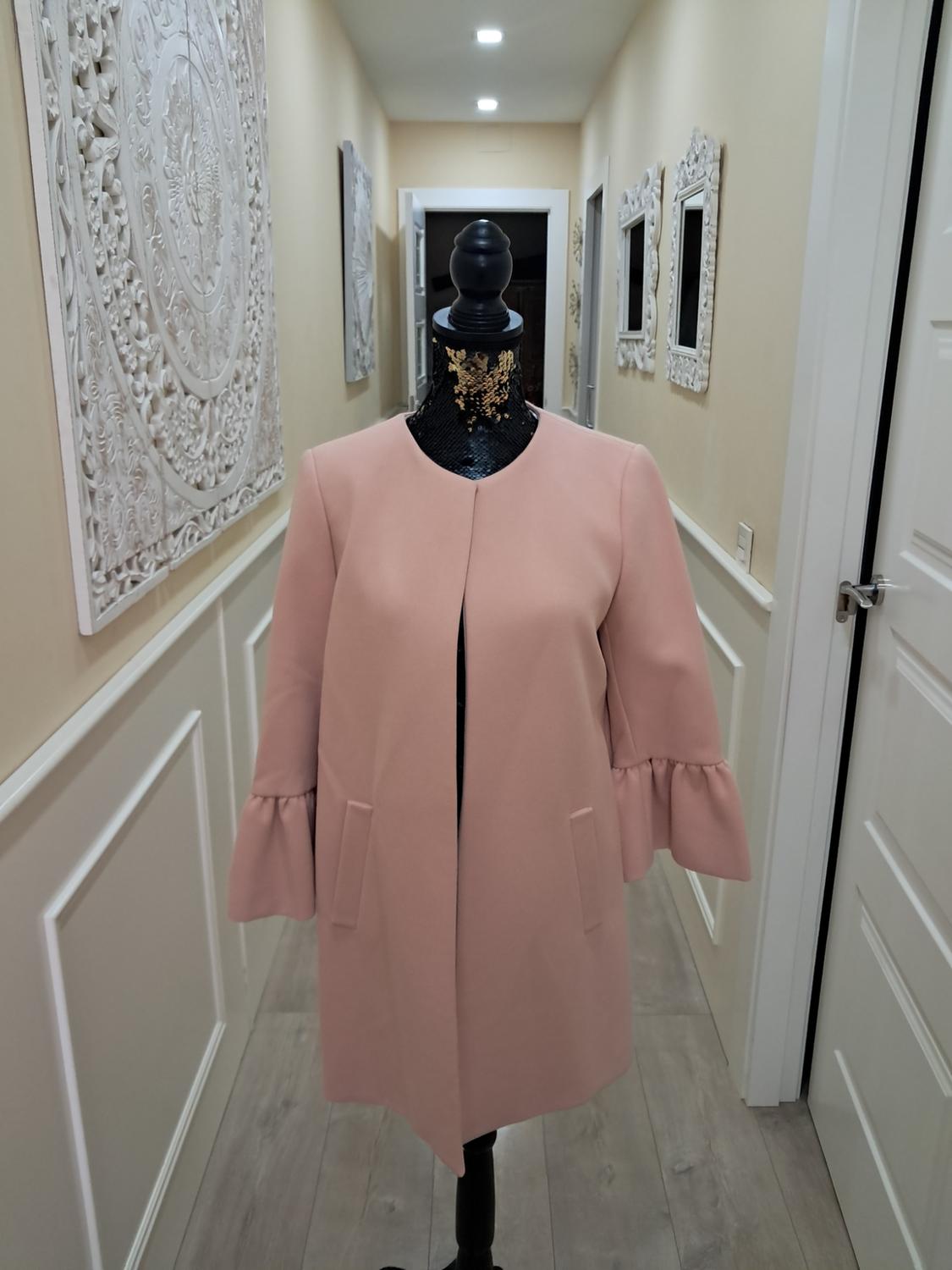 Mannequin in a long-sleeved, ruffled pink coat in a hallway decorated with white panels and mirrors.
